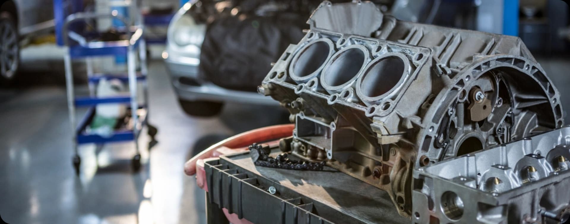 Close-up of a disassembled car engine block with exposed cylinders in a mechanic's workshop.