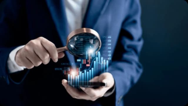 Businessman examining glowing holographic financial bar chart with magnifying glass.