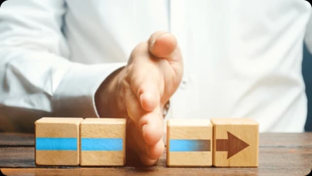 Businessman's hand pushing wooden blocks with blue lines and a directional arrow.