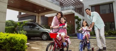A happy family of four with two young girls riding bicycles outside a modern home.